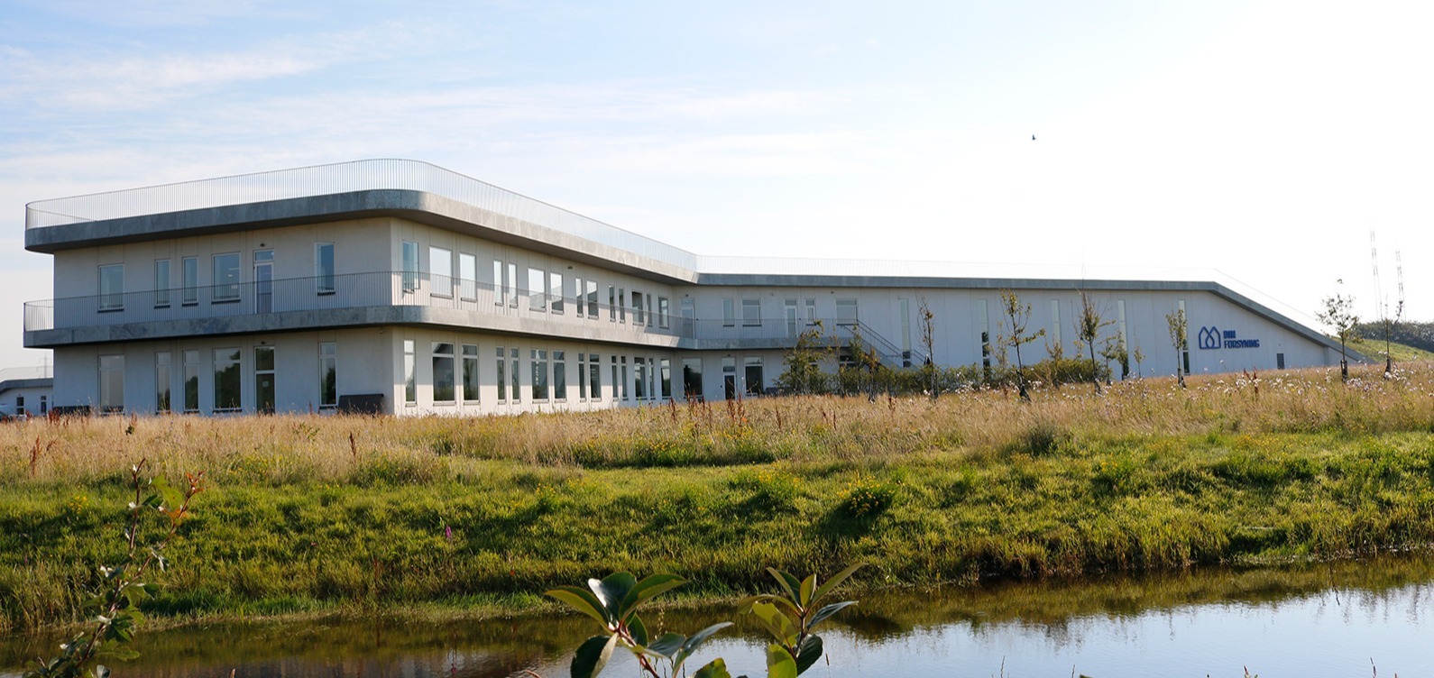 Modern Din Forsyning facility with glass facade and grass in foreground. Modern Din Forsyning facility with glass facade and grass in foreground.